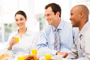 Happy multi-ethnic business people at table looking away while having breakfast together. Horizontal shot.